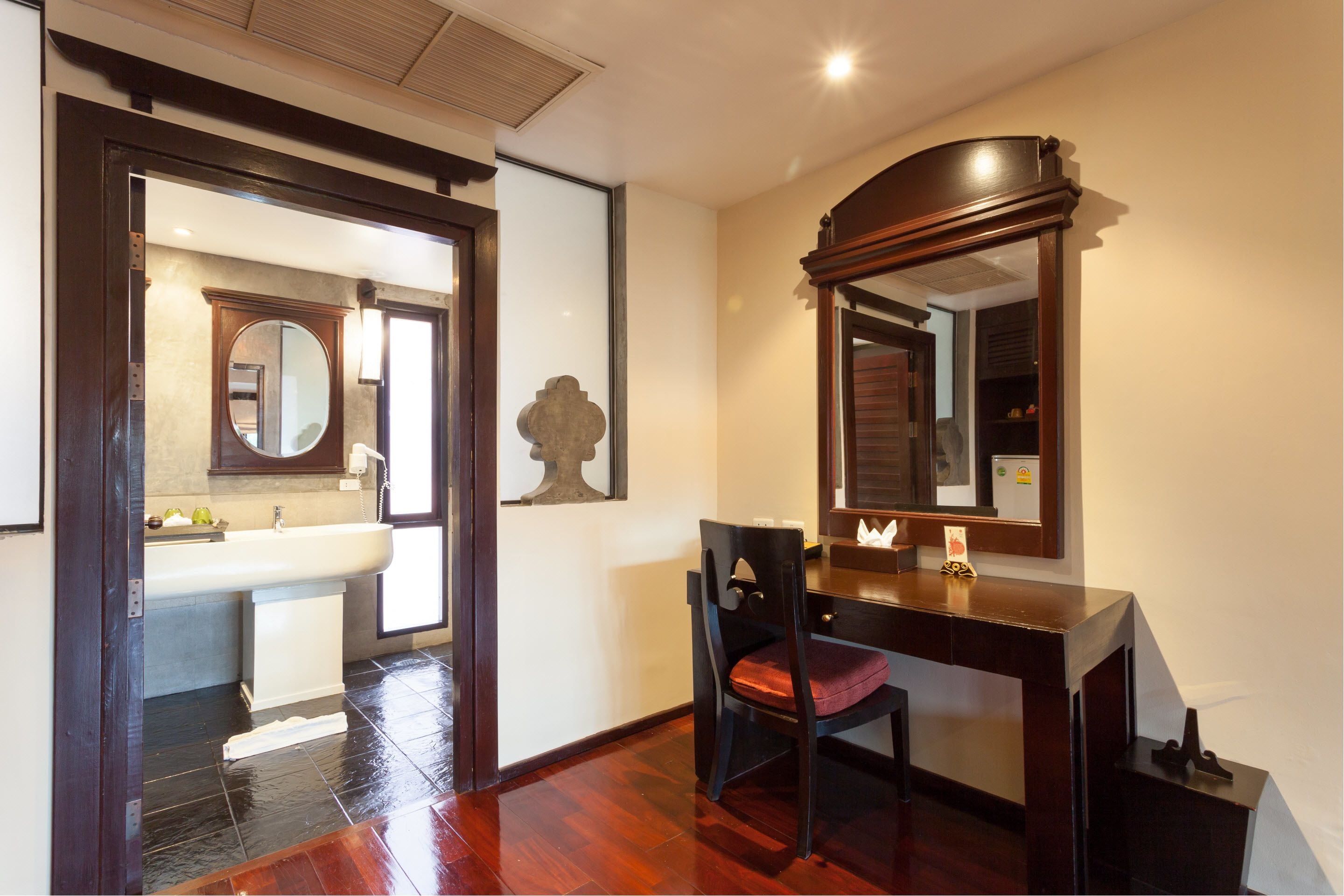 A hotel room with a wooden desk, a chair, a large mirror, and a view of the bathroom.