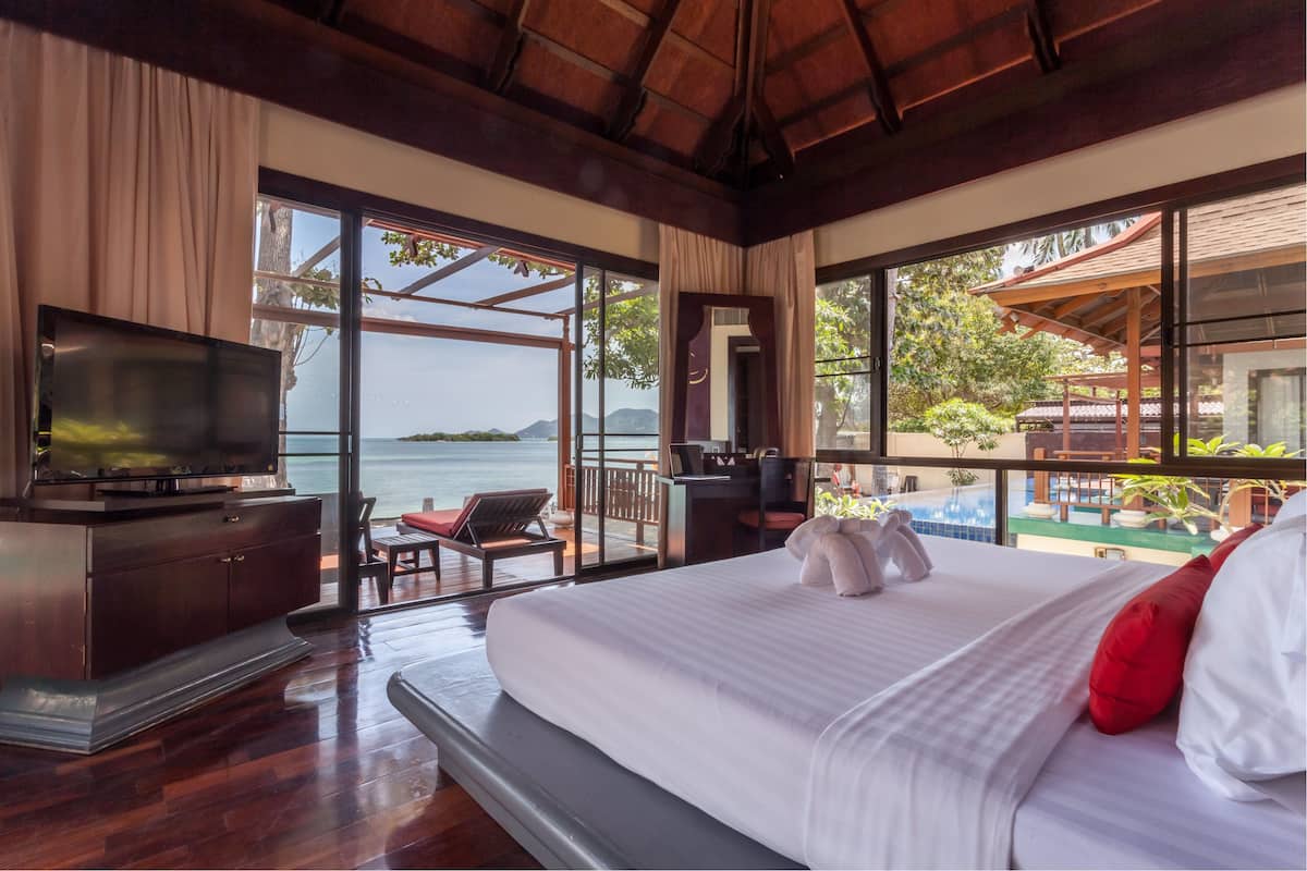A hotel room with a large bed, a TV, a desk, and a view of the sea.