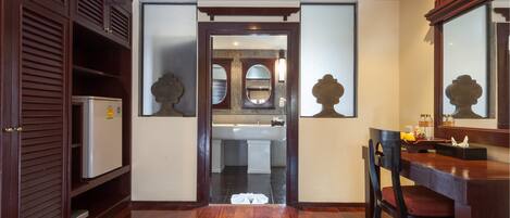 A hallway leading to a bathroom with a sink and mirror, wooden flooring, and a refrigerator.