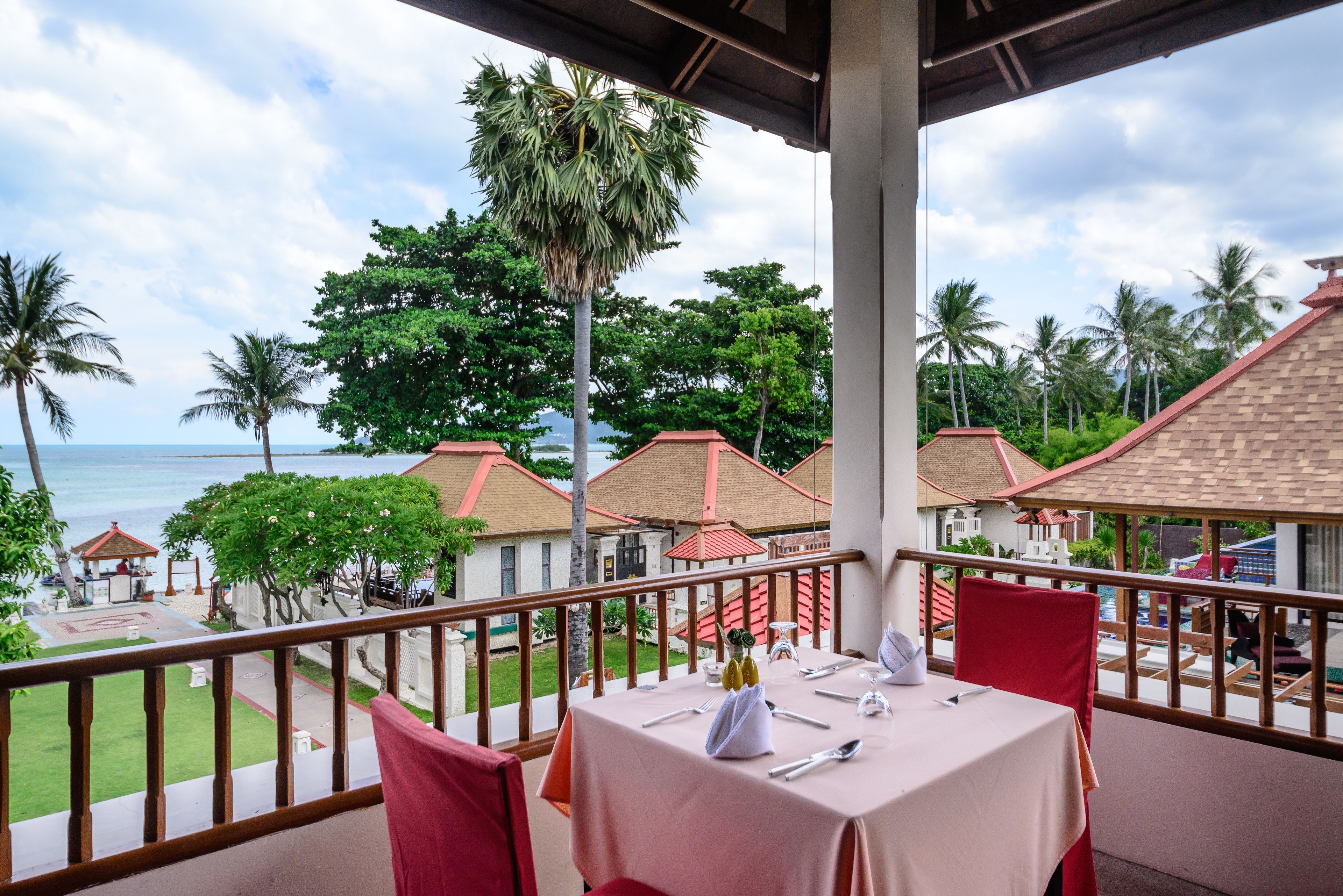 Un balcón con mesa lista para comer, con vista a una playa y palmeras.