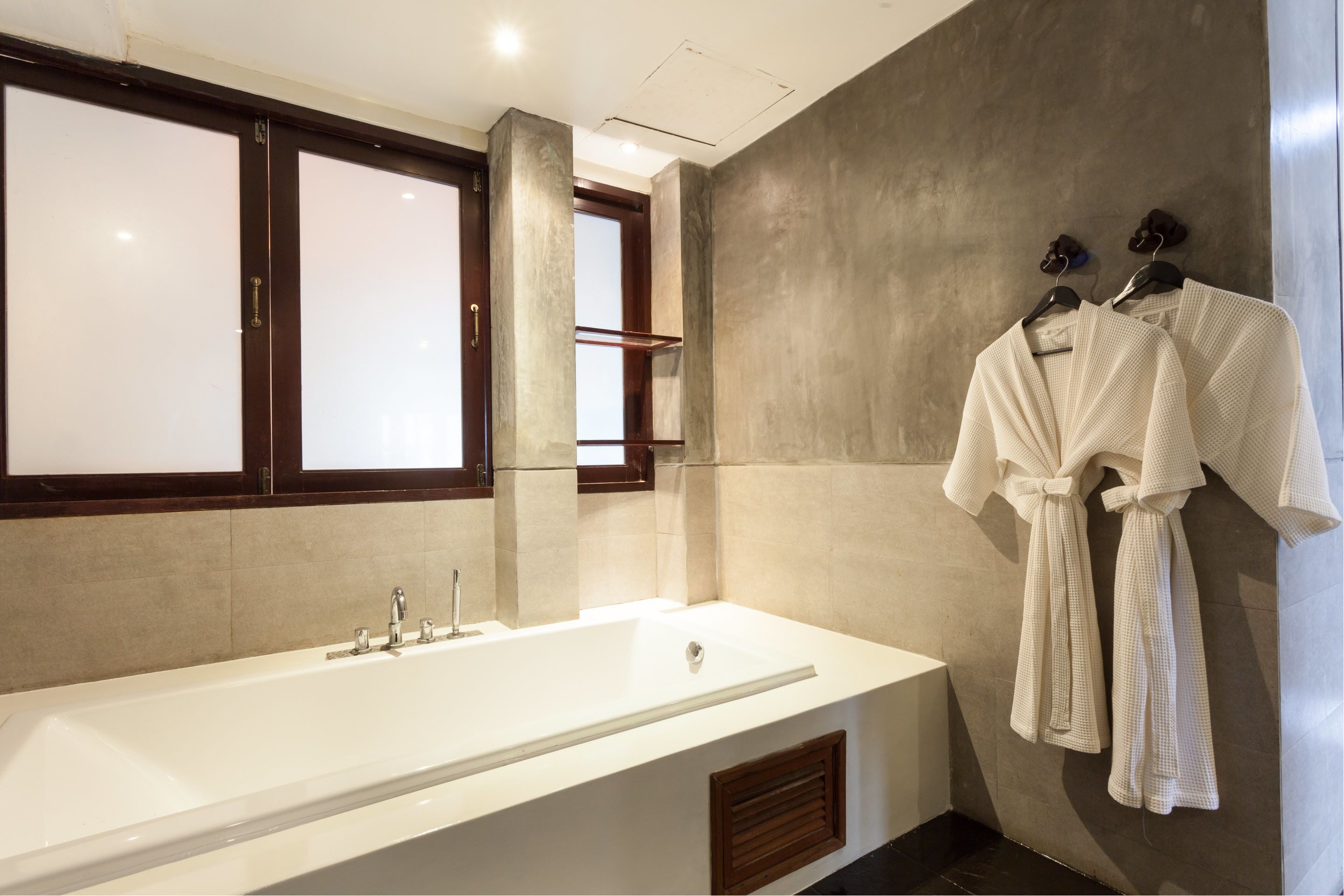 Un baño moderno con una bañera grande, una ventana con vidrio esmerilado y un perchero con albornoces.
