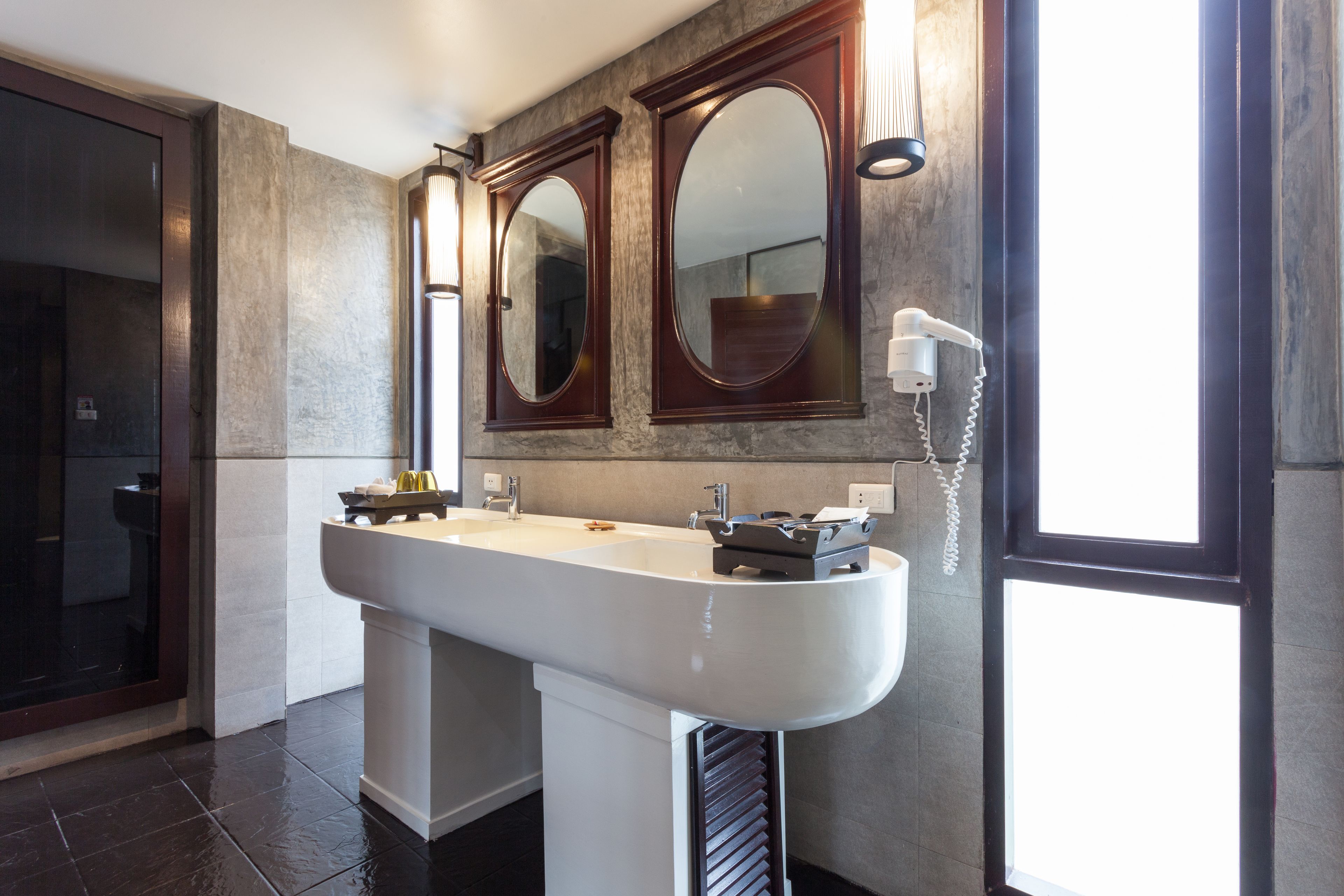 A modern bathroom with a large sink, two mirrors, and a hairdryer on the wall.