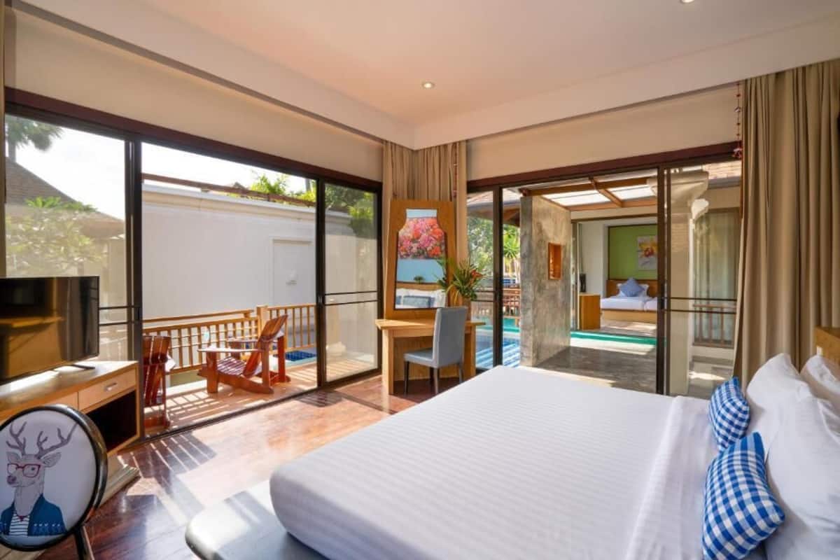 A spacious bedroom with a large bed, a desk, and a chair. There is a balcony with a pool view.