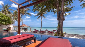 A poolside area with lounge chairs and umbrellas, overlooking a beach with palm trees and a clear sky.