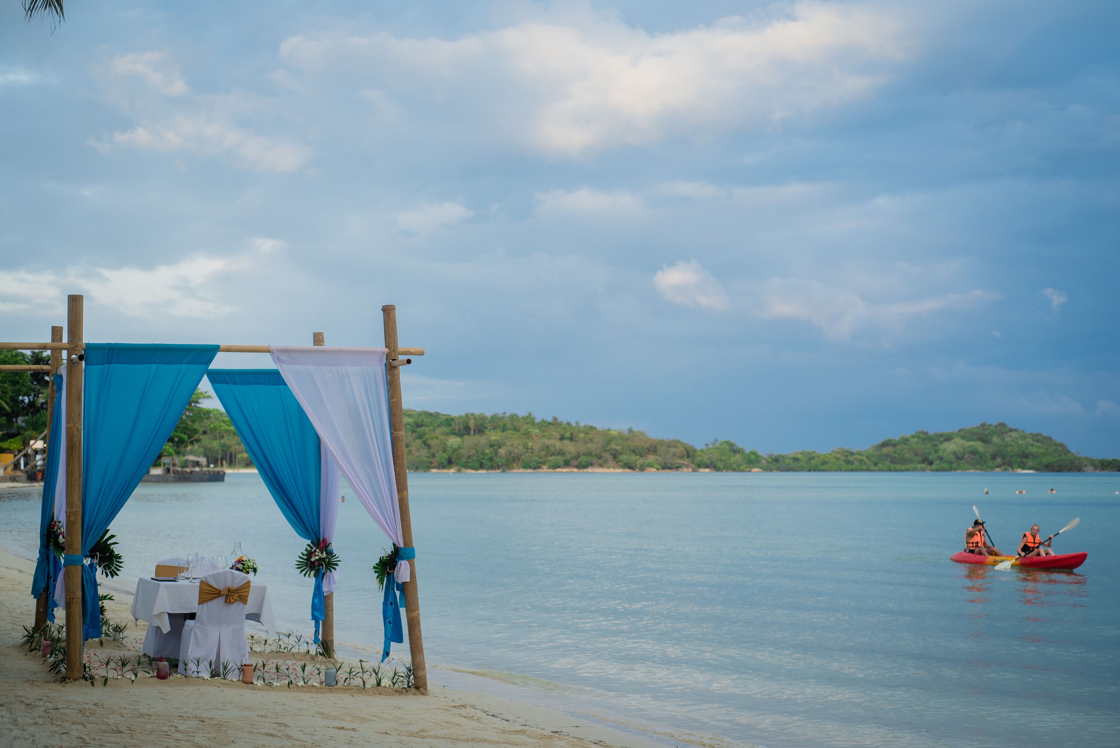 Une cérémonie de mariage organisée sur la plage, avec un dais et une table, offrant une vue sur des eaux calmes et une île lointaine.