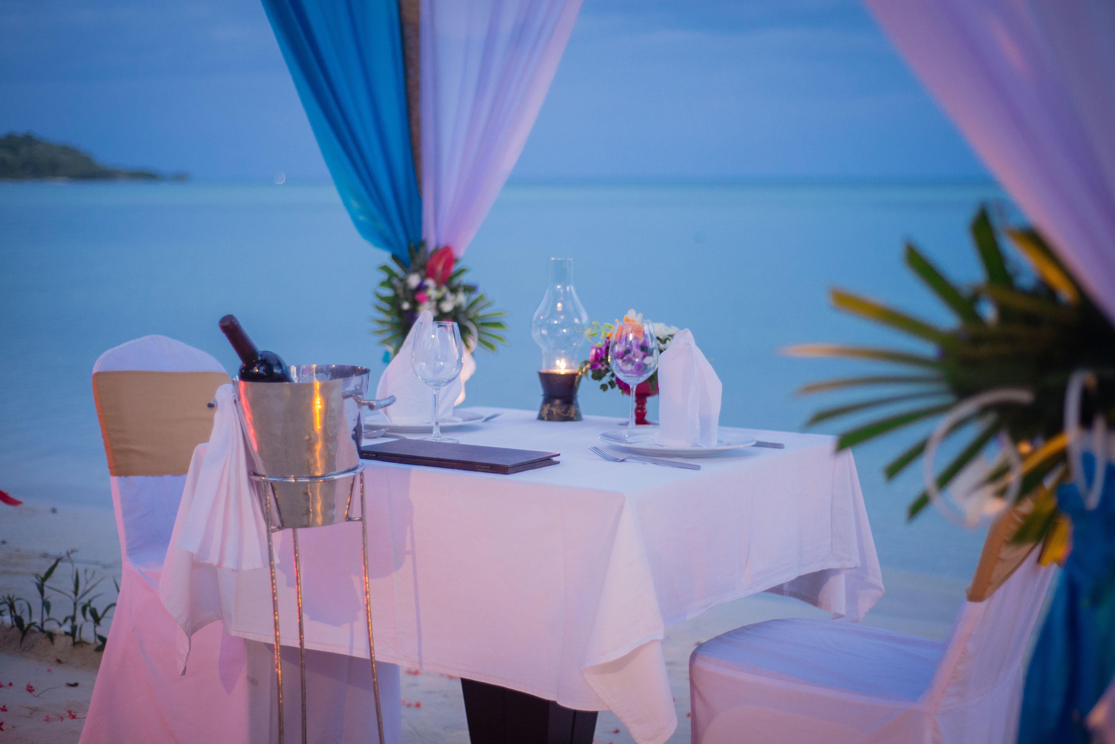 Une table dressée pour deux personnes, avec vue sur la mer, une bouteille, des verres et une bougie.