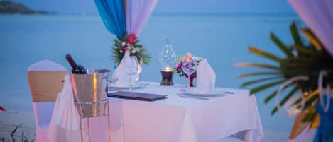 Une table dressée pour deux personnes, avec vue sur la mer, une bouteille, des verres et une bougie.