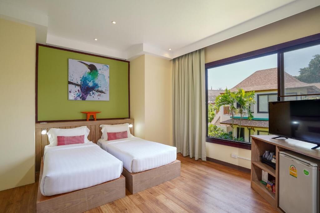 A hotel room with two beds, a television, a painting, and a view of the outside.