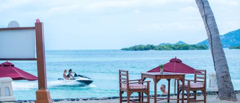 Una mesa y sillas frente a la playa, con vista al océano y un barco al fondo.