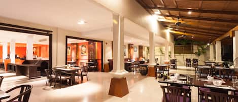 A spacious hotel lobby with multiple dining areas, a reception desk, and a view of the outdoor area.
