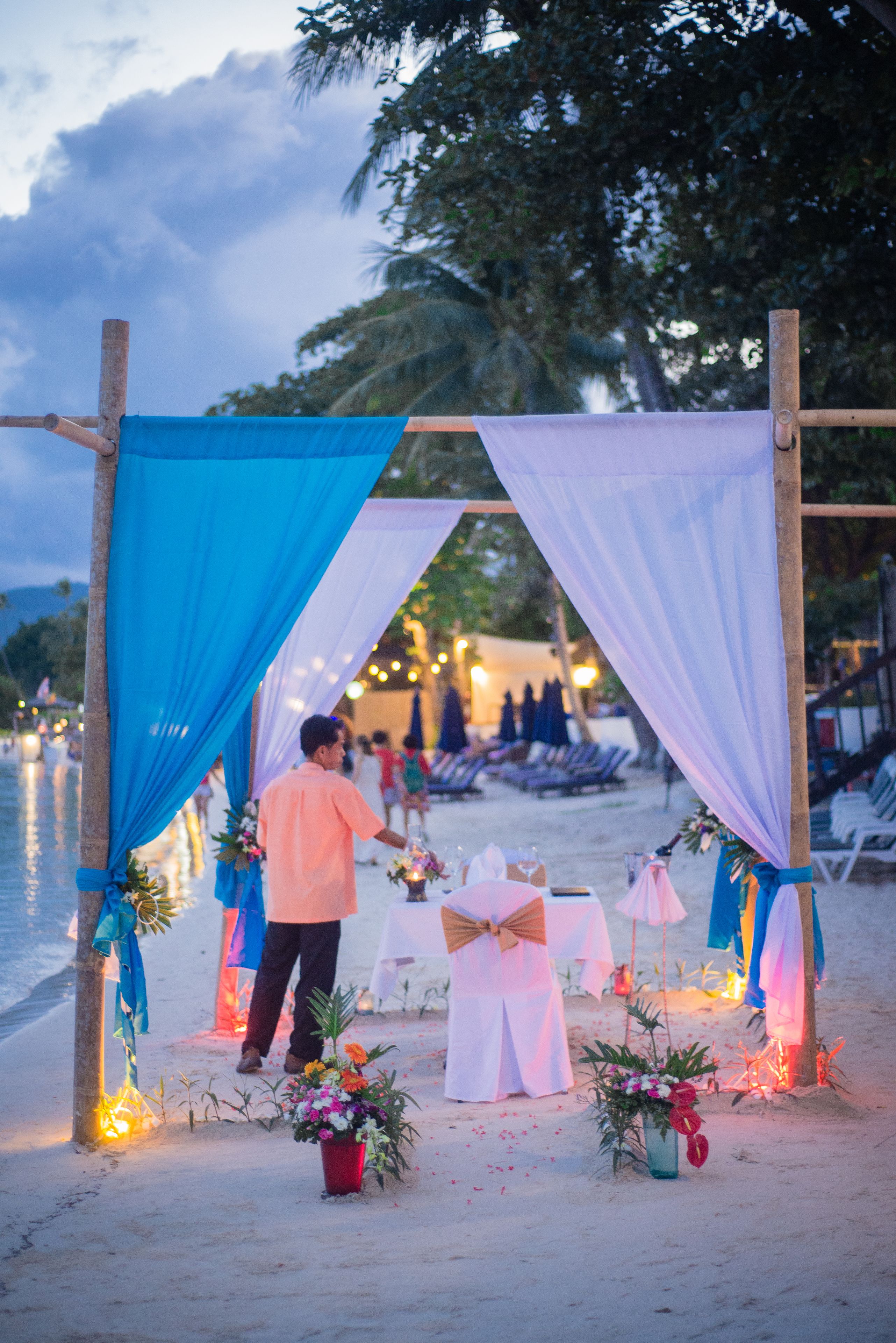 A beachside wedding setup with a wooden arch, tables, and floral decorations.