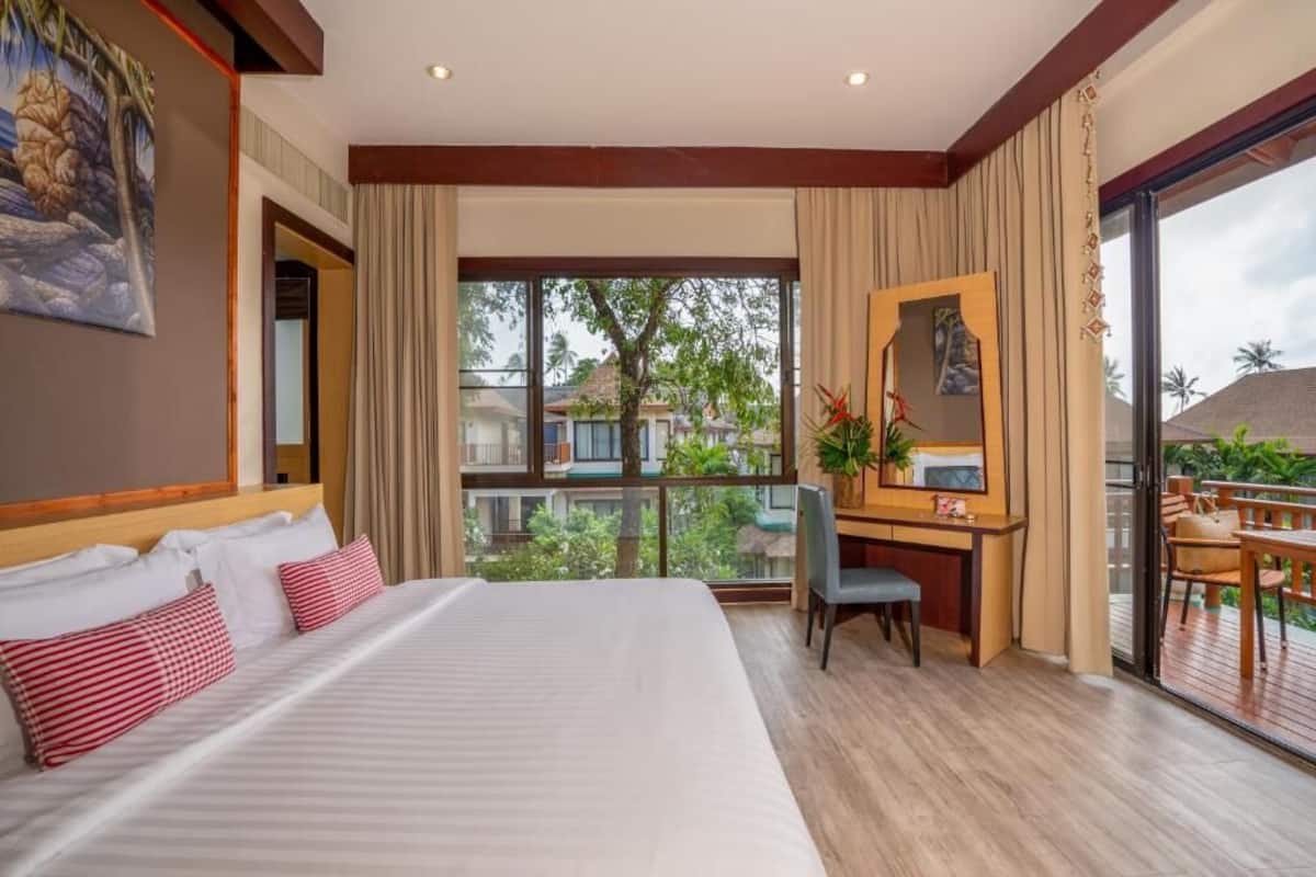 A hotel room with a large bed, a desk, and a balcony with a view of the surrounding area.