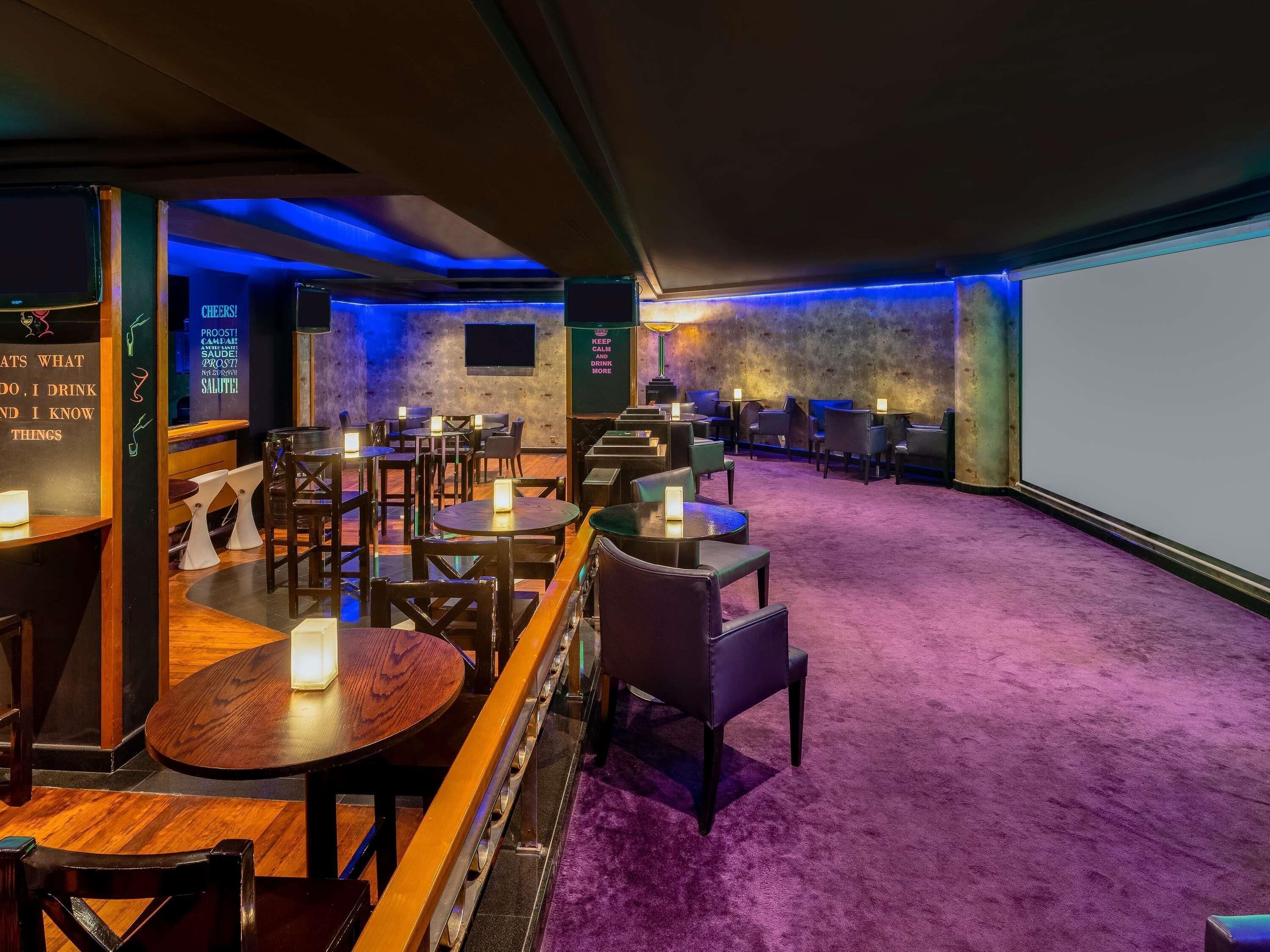 A dimly lit room with tables and chairs, a projector screen, and a wall with motivational quotes.