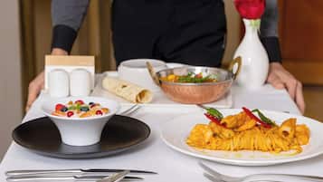 A table set with breakfast items including a bowl of cereal, a rolled pastry, and a plate of food, with a vase of red roses in the background.