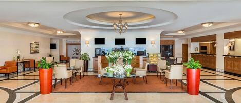 A hotel lobby with a reception desk, seating area, and a bar.