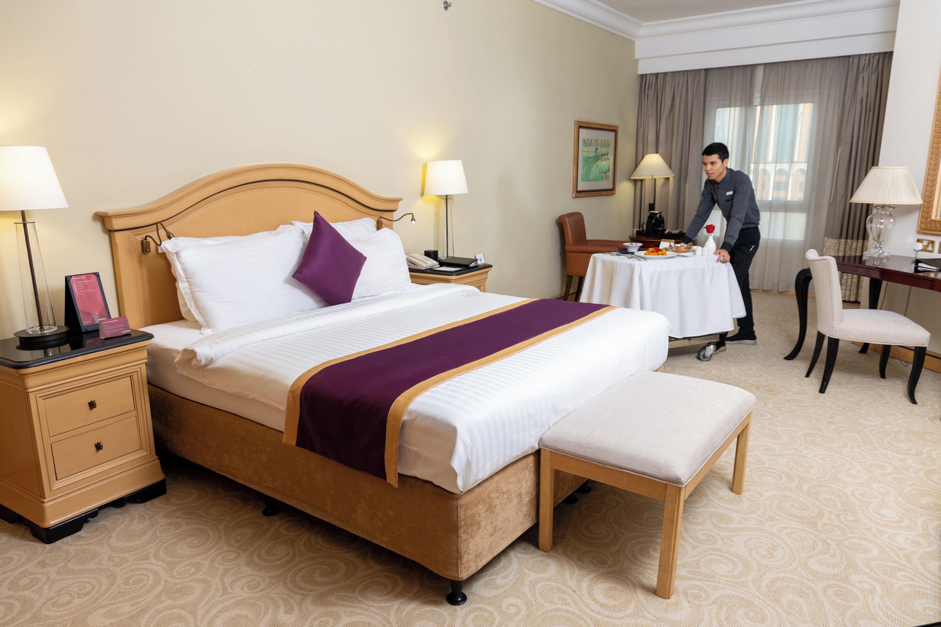 Una habitación de hotel con una cama grande, una mesita de noche, un escritorio, una silla y una pequeña mesa con una lámpara de pie.