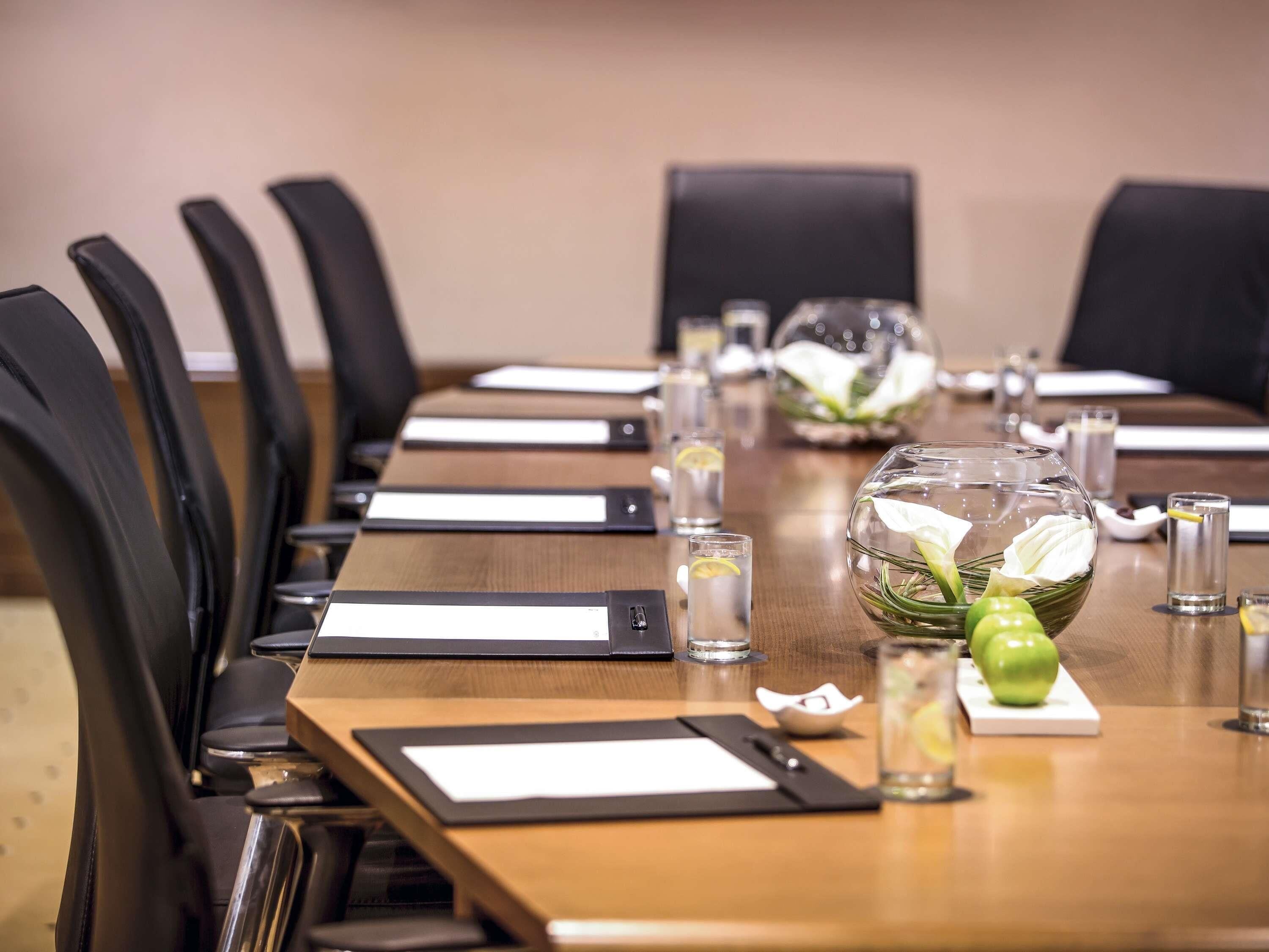 A conference room with a long table, black chairs, nameplates, water glasses, and a decorative bowl with flowers.