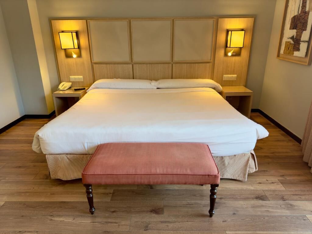 Habitación de hotel con una cama grande, lámparas de noche, un teléfono y suelo de madera.