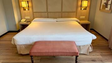 Habitación de hotel con una cama grande, lámparas de noche, un teléfono y suelo de madera.