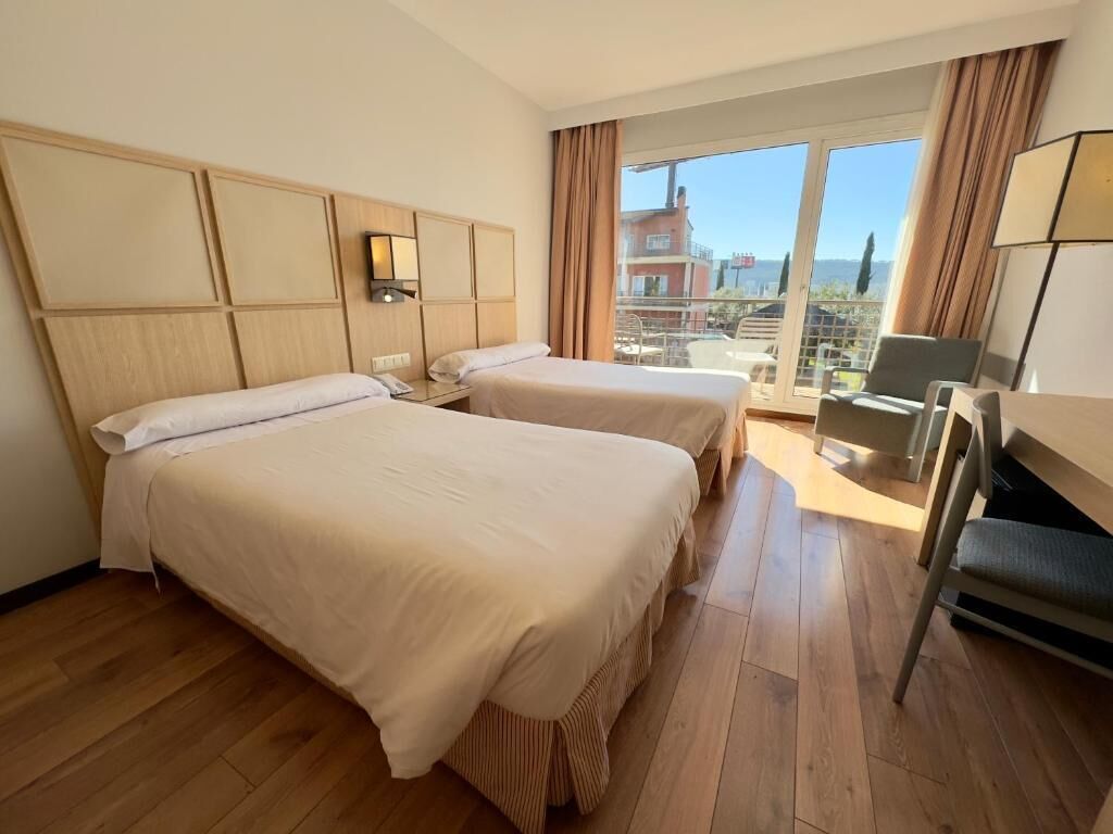 A hotel room with two beds, a desk, and a view of the city.