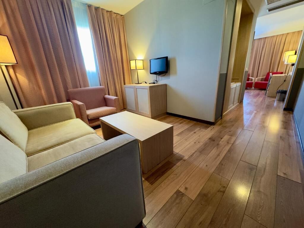 Une chambre d’hôtel avec un canapé, une petite table, un téléviseur et un bureau avec une lampe.