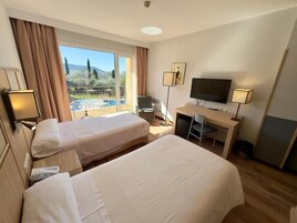 Habitación de hotel con dos camas, un escritorio, un televisor y vista a una piscina.