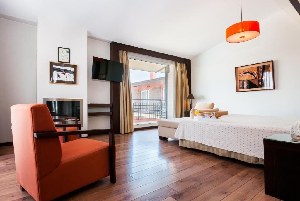 Une chambre d’hôtel avec un lit, une chaise, une télévision et un balcon avec des rideaux.