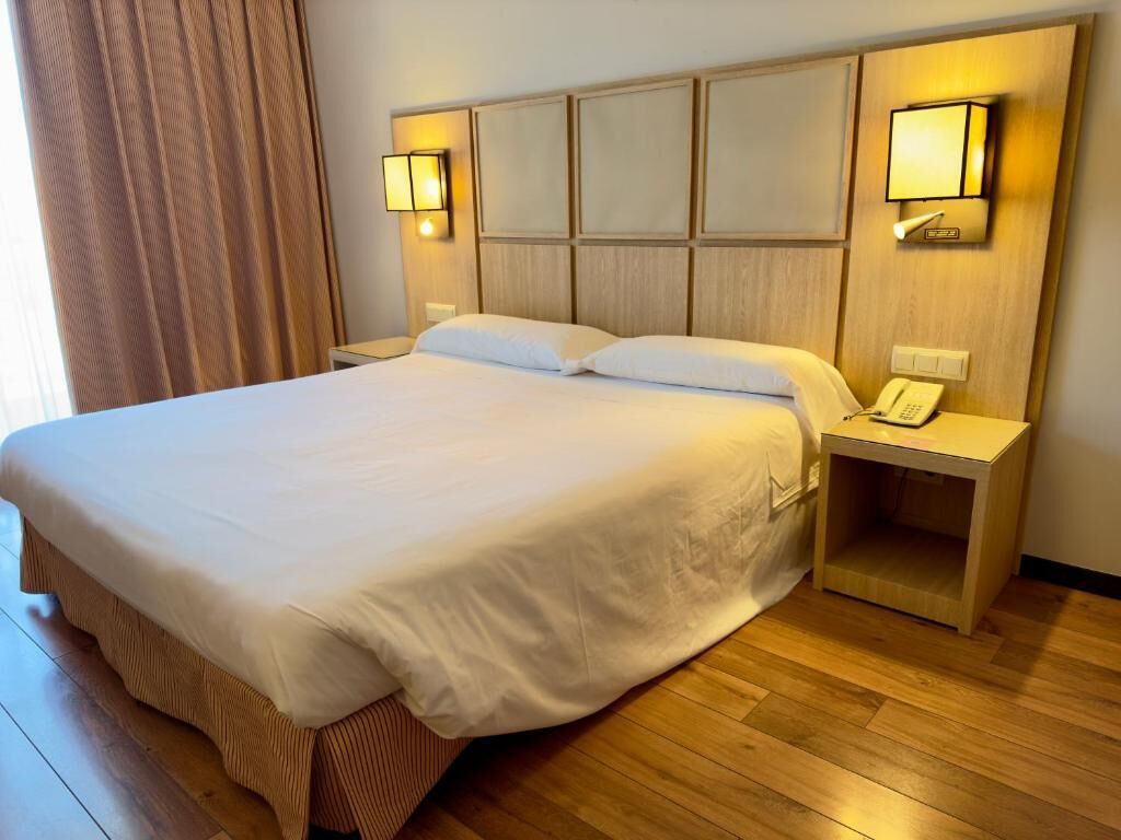 Ein Hotelzimmer mit einem großen Bett, zwei Nachttischen und einer Kopfteil mit Wandlampen.