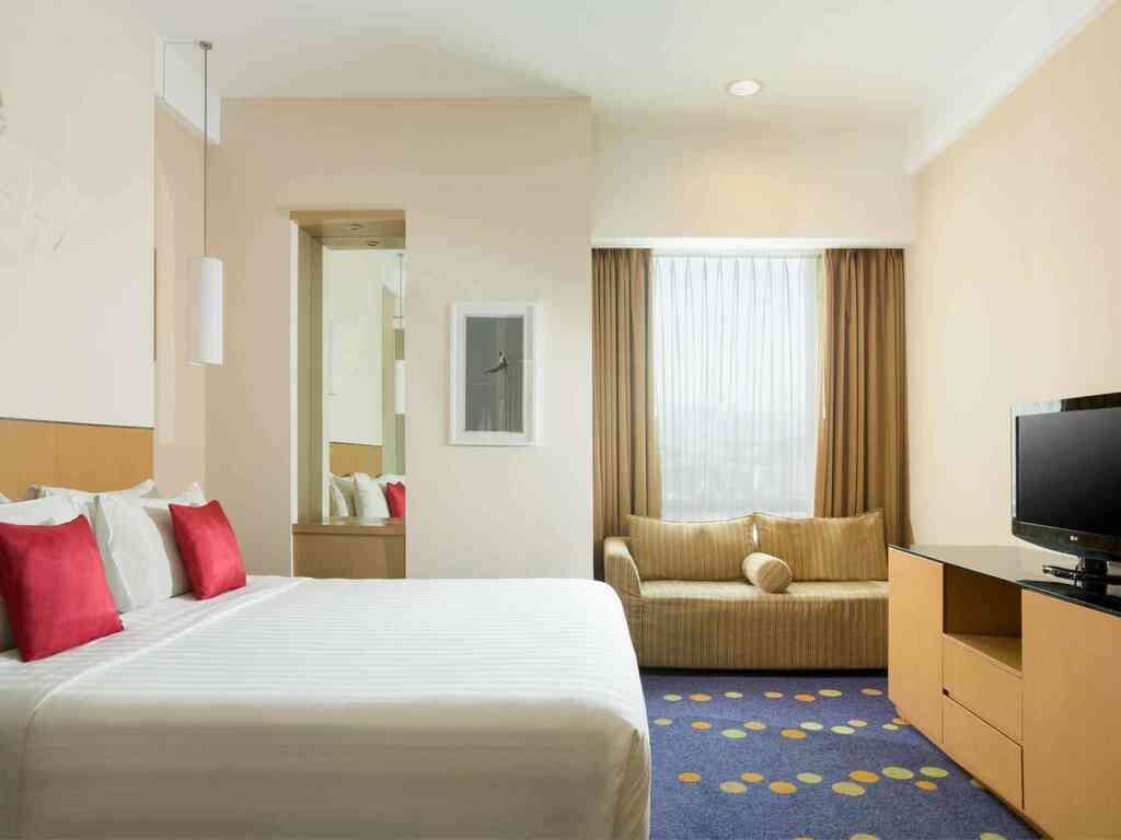 Ein Hotelzimmer mit Bett, Sofa, Fernseher und einem durchgegangenen Tür sichtbaren Badezimmer.
