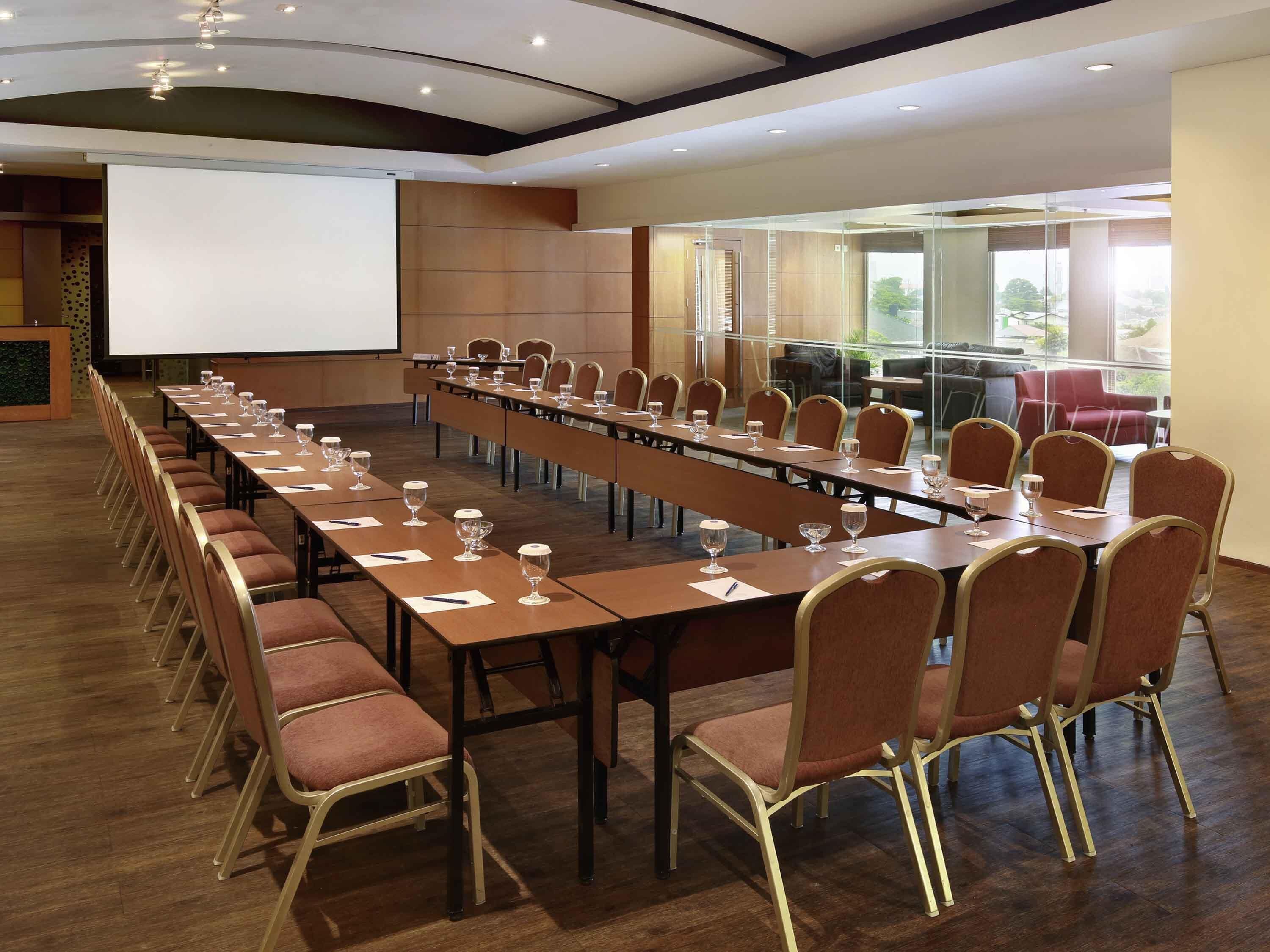 A conference room with long tables, chairs, and a projector screen.