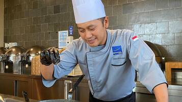 A chef in a professional kitchen with a tiled backsplash, stainless steel appliances, and a buffet setup.