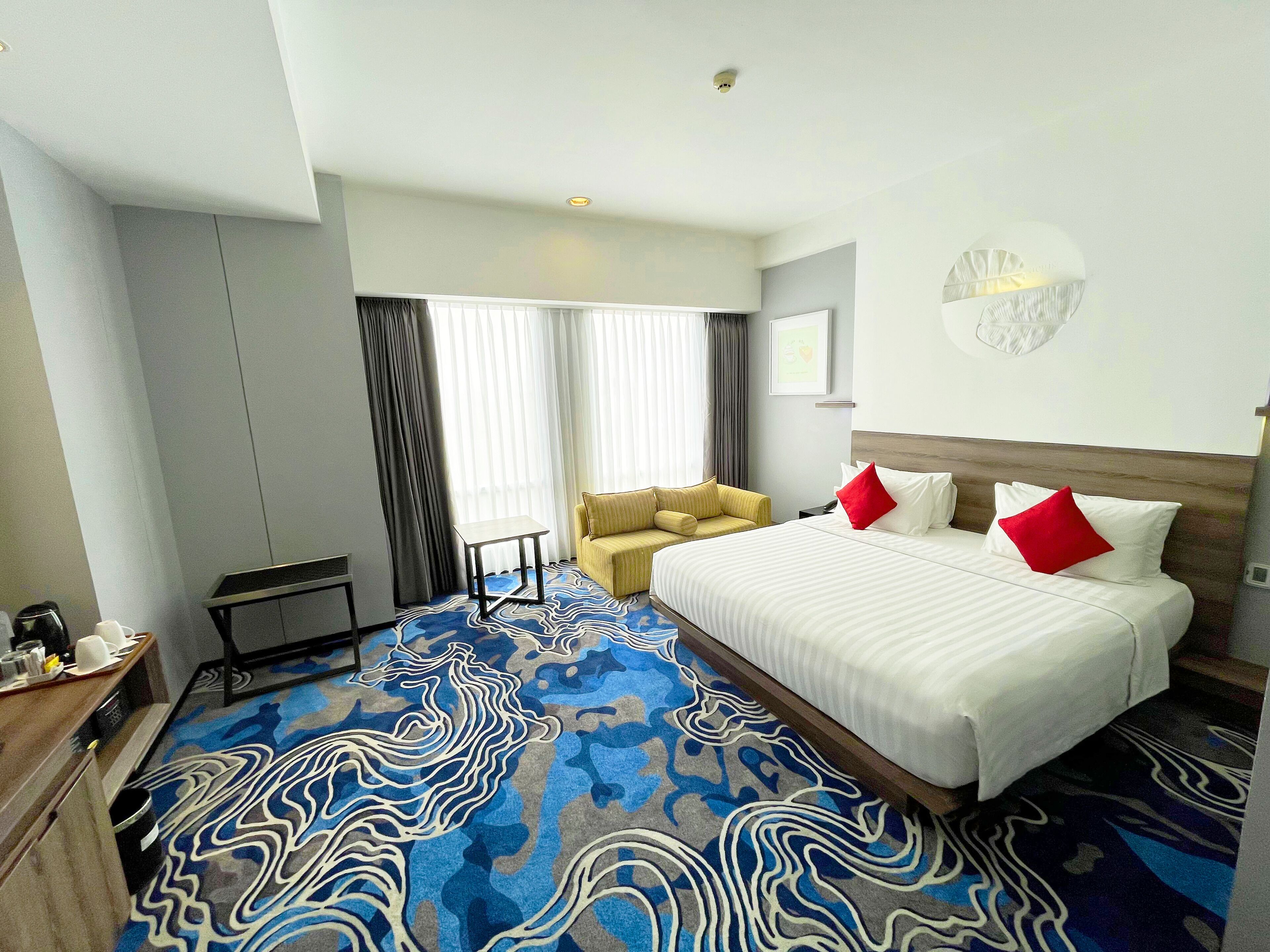 Una habitación de hotel con una cama grande, un sofá, una mesita y una alfombra estampada.