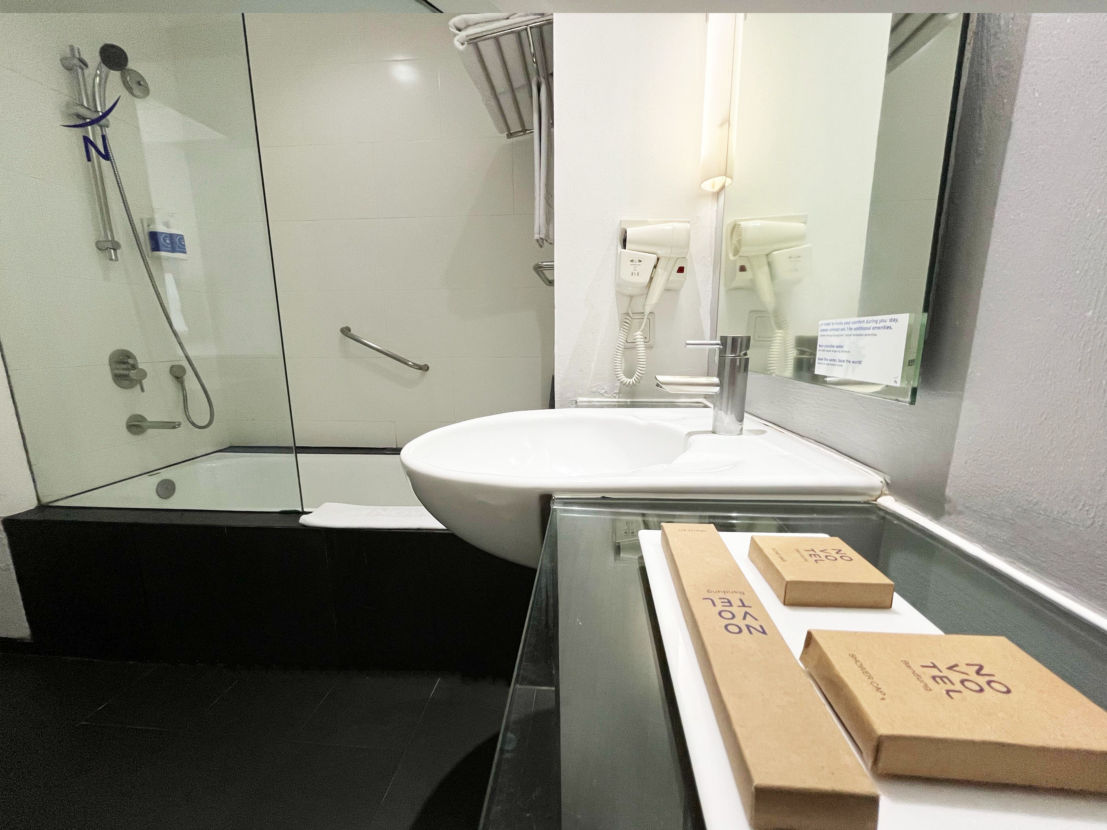 A modern bathroom with a glass-enclosed shower, a white sink, and a mirror. There are two brown boxes on the counter.