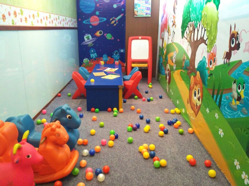 A children's playroom with colorful balls scattered on the floor, a table with chairs, and a mural with animal characters.
