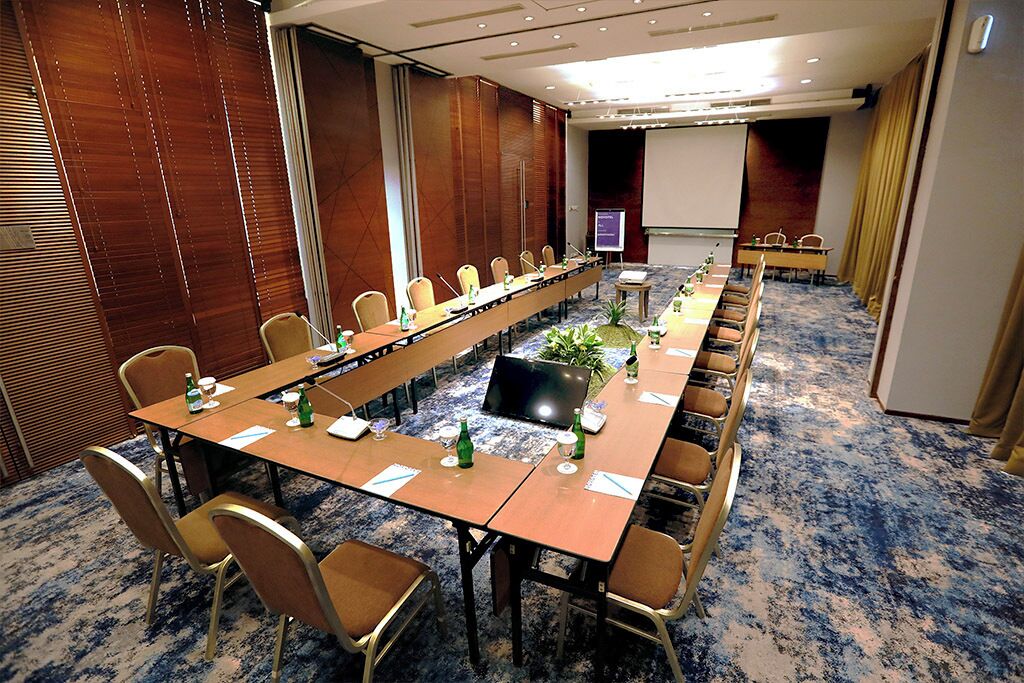 A conference room with a long table, chairs, a projector screen, and a carpeted floor.