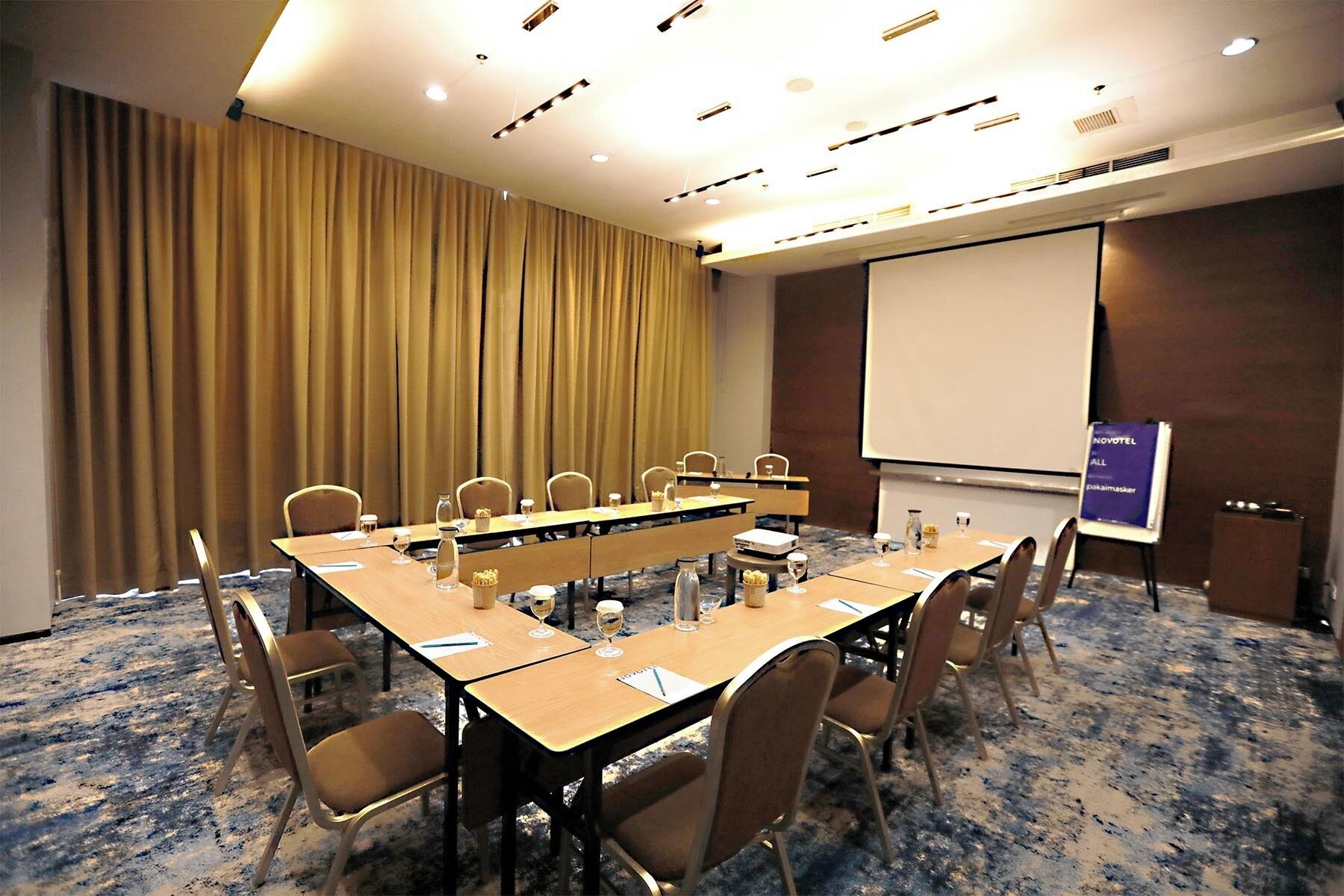 A conference room with a long table, chairs, a projector screen, and a presentation board.