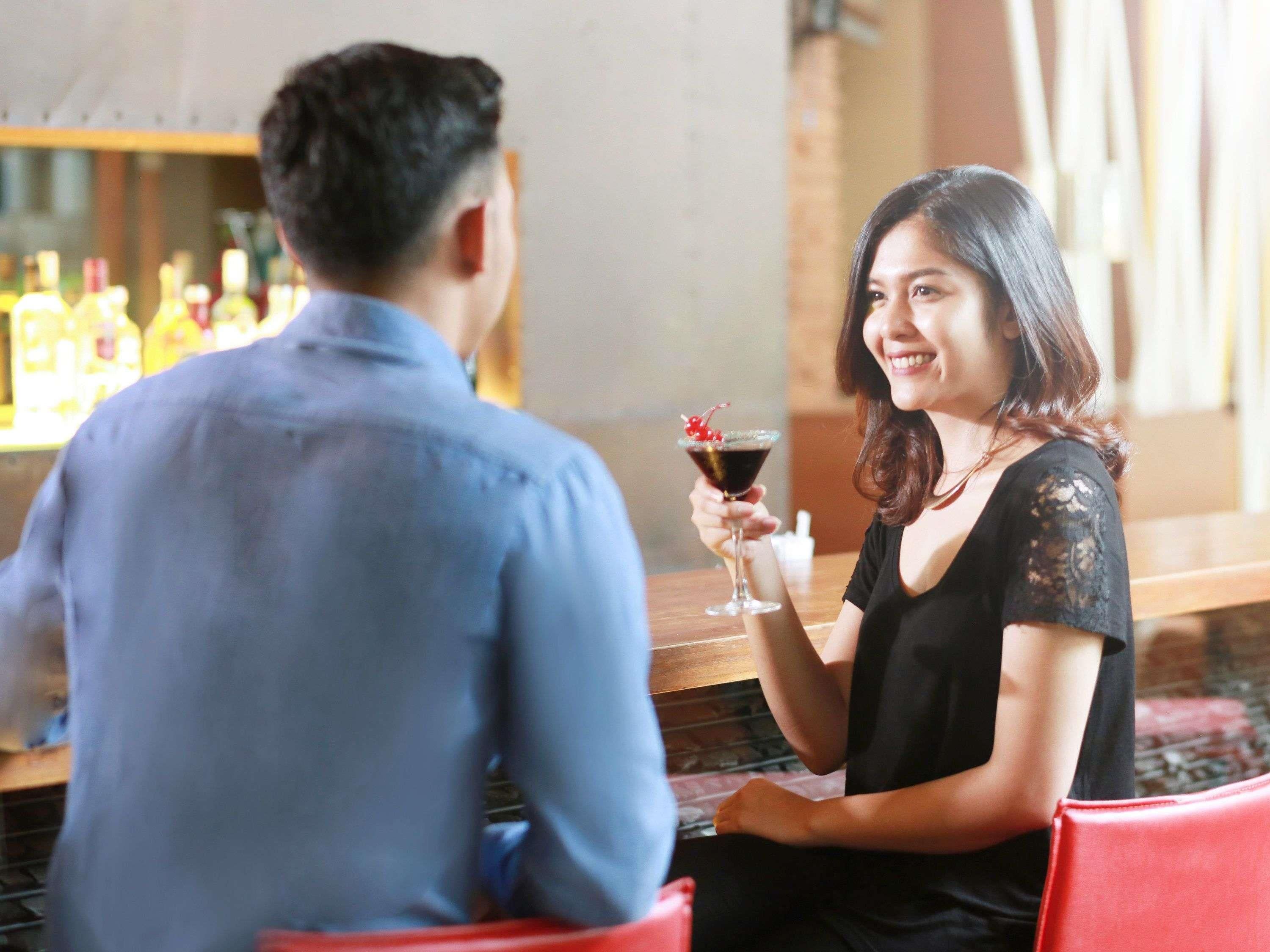 Una persona sosteniendo una bebida en un bar, con botellas al fondo.