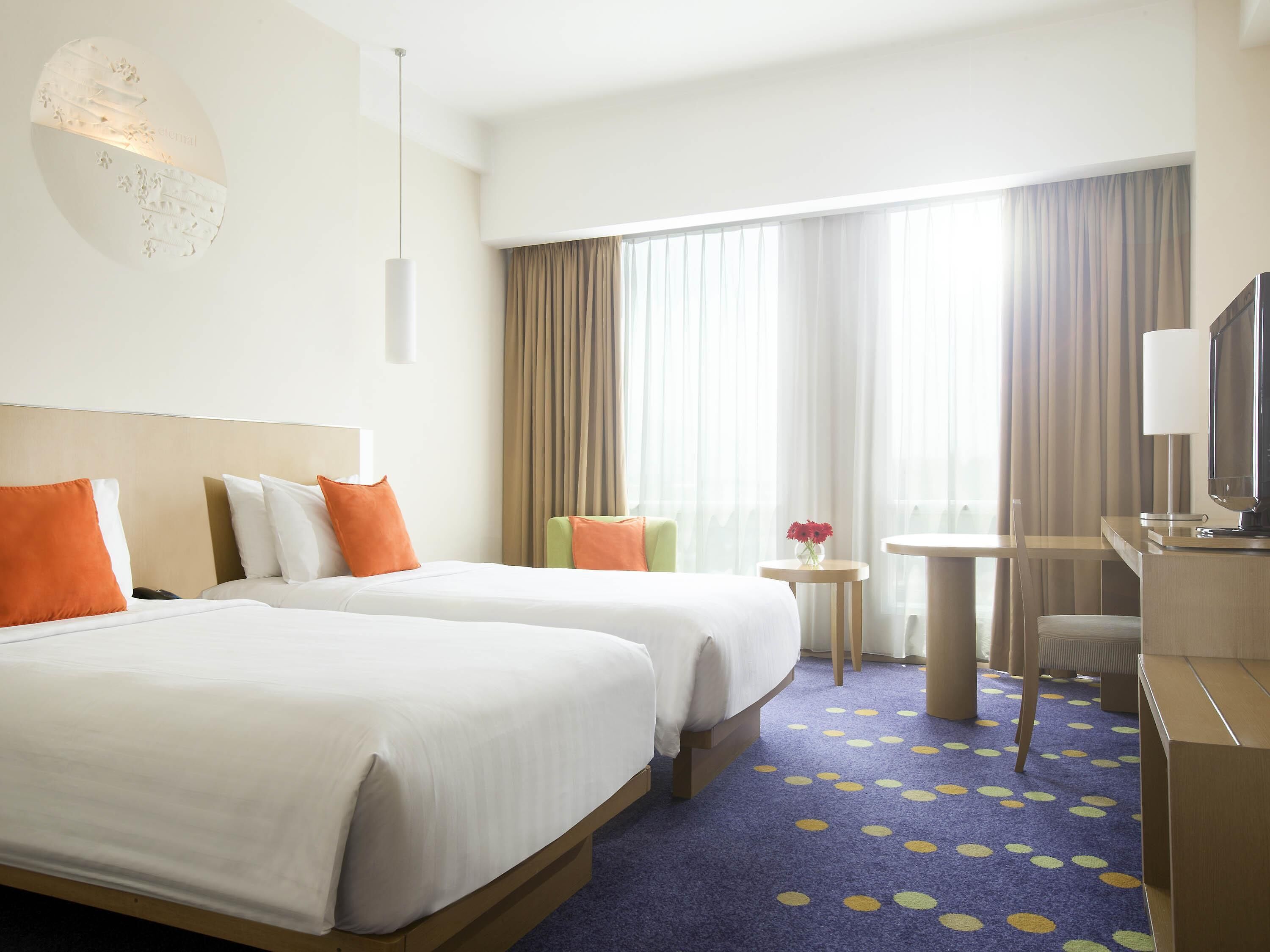 A hotel room with two beds, a desk, a chair, a TV, and a window with curtains.