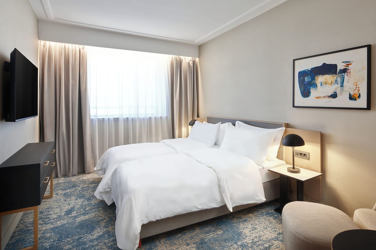A hotel room with a bed, a desk, a TV, and a painting on the wall.