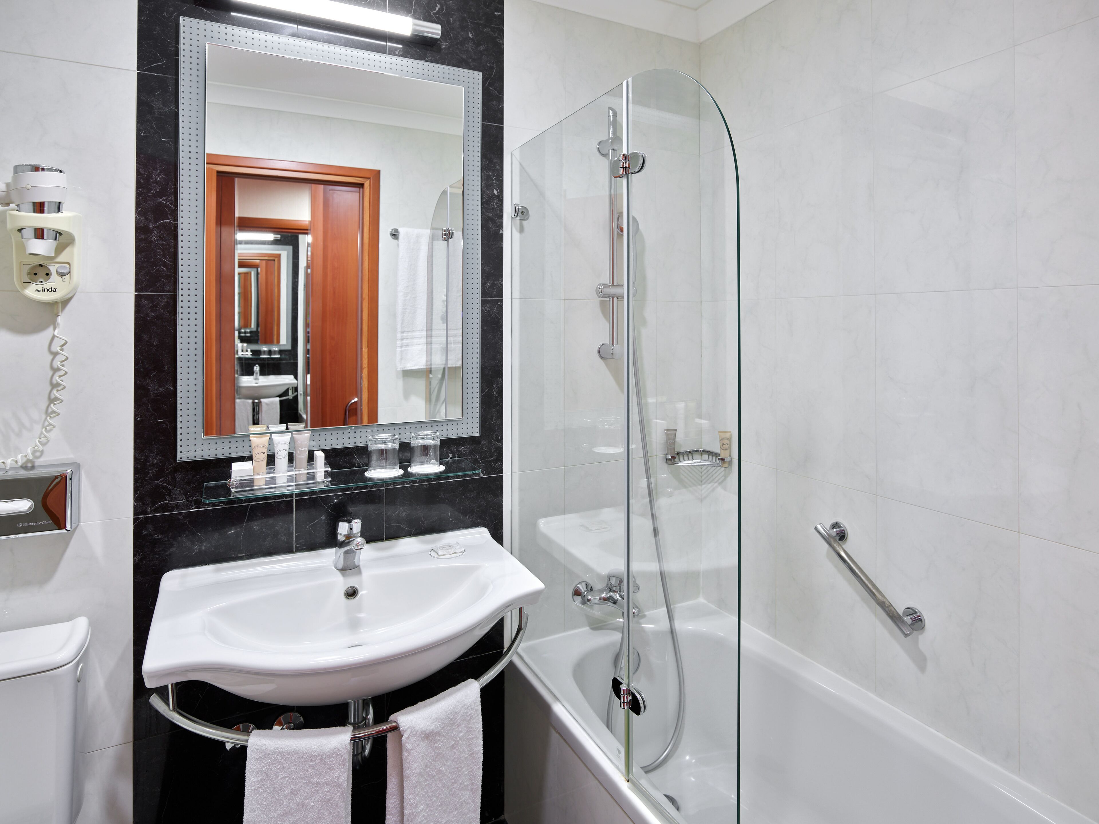 A modern bathroom with a glass-enclosed shower, a white sink, and a large mirror.