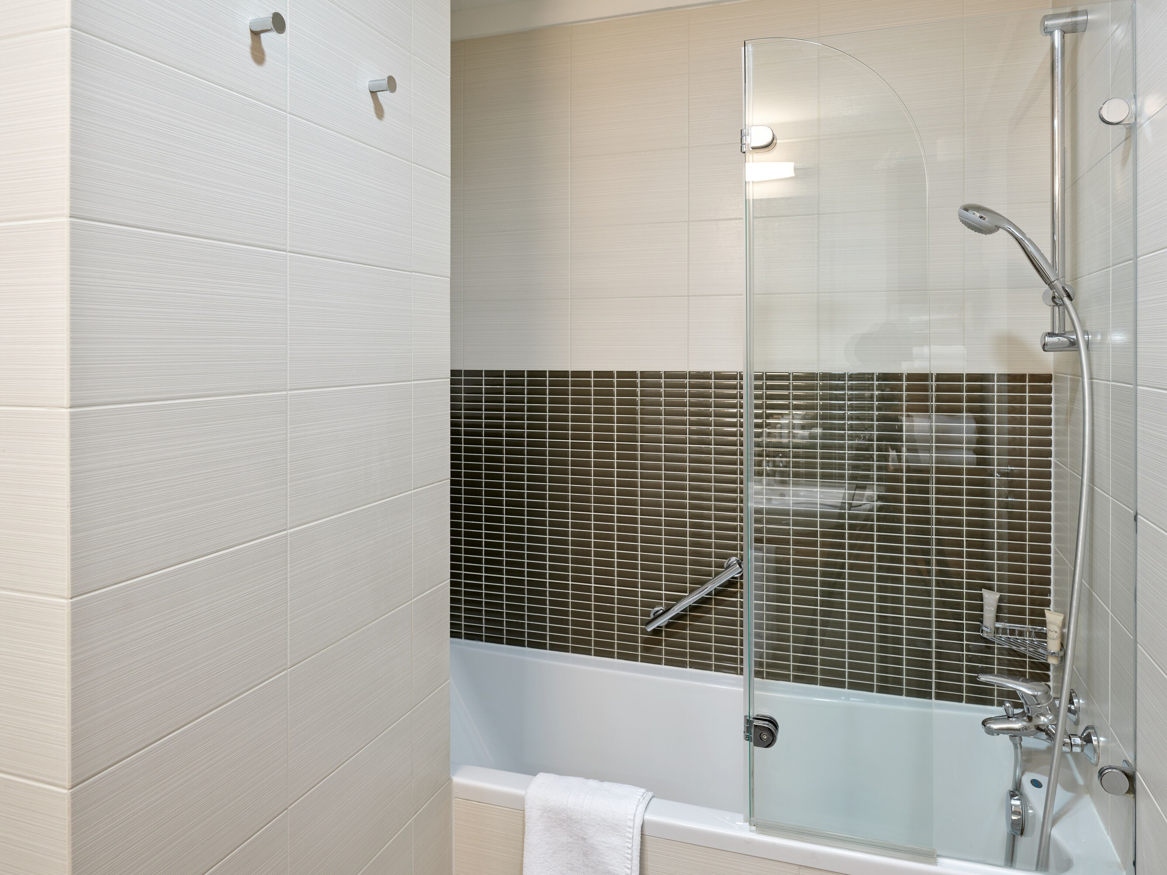 A modern bathroom with a glass-enclosed shower, a bathtub, and a tiled wall with a grid pattern.