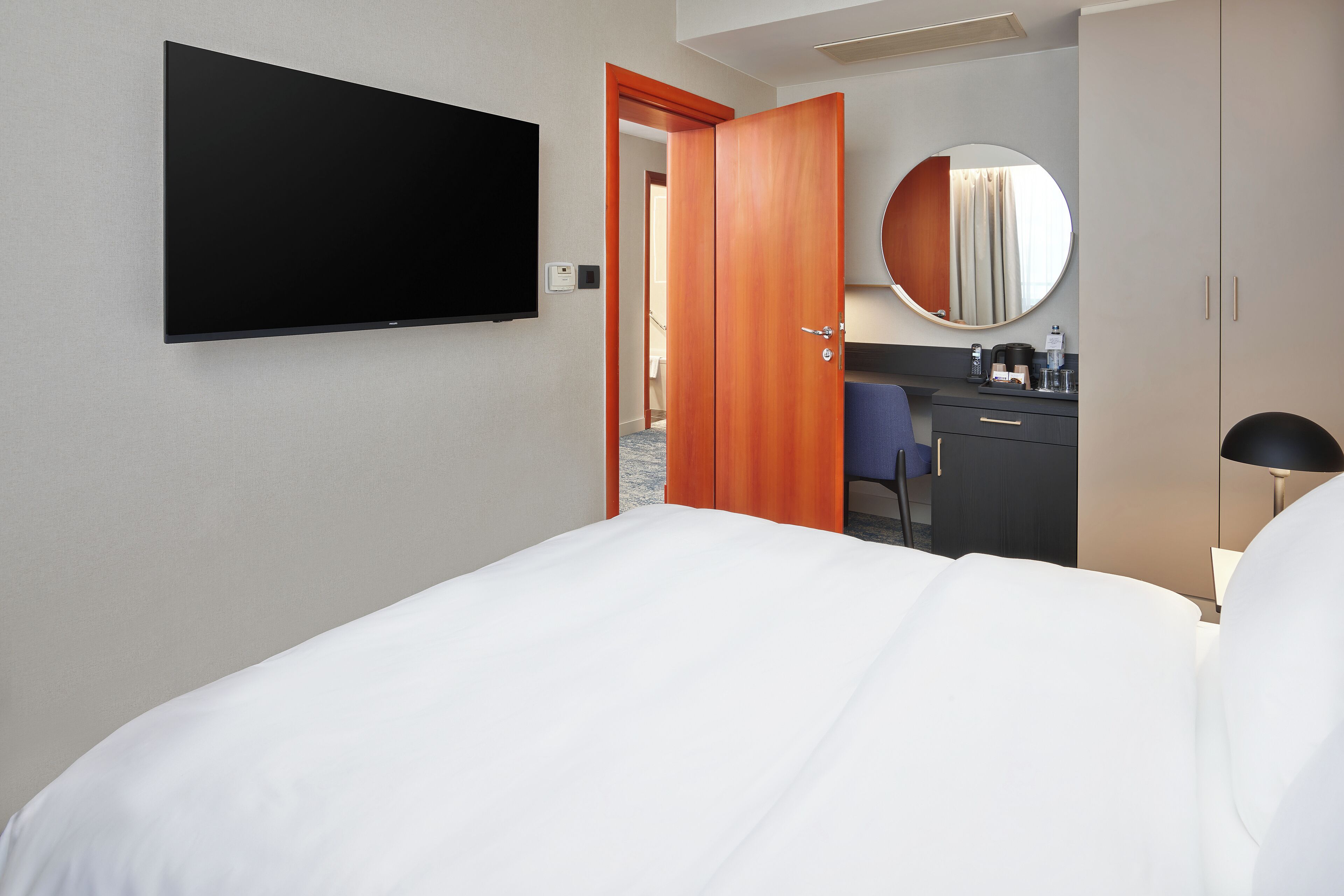 Une chambre d’hôtel comprenant un lit, une télévision, un bureau avec une chaise, un miroir et une armoire.