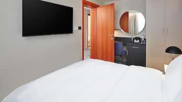 A hotel room with a bed, a TV, a desk with a chair, a mirror, and a wardrobe.