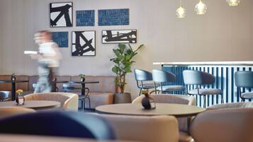 A modern restaurant with round tables and blue chairs, a bar area, and abstract wall art.