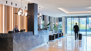 Un área de recepción moderna con un mostrador de mármol, zona de estar y grandes ventanales con vistas al exterior.
