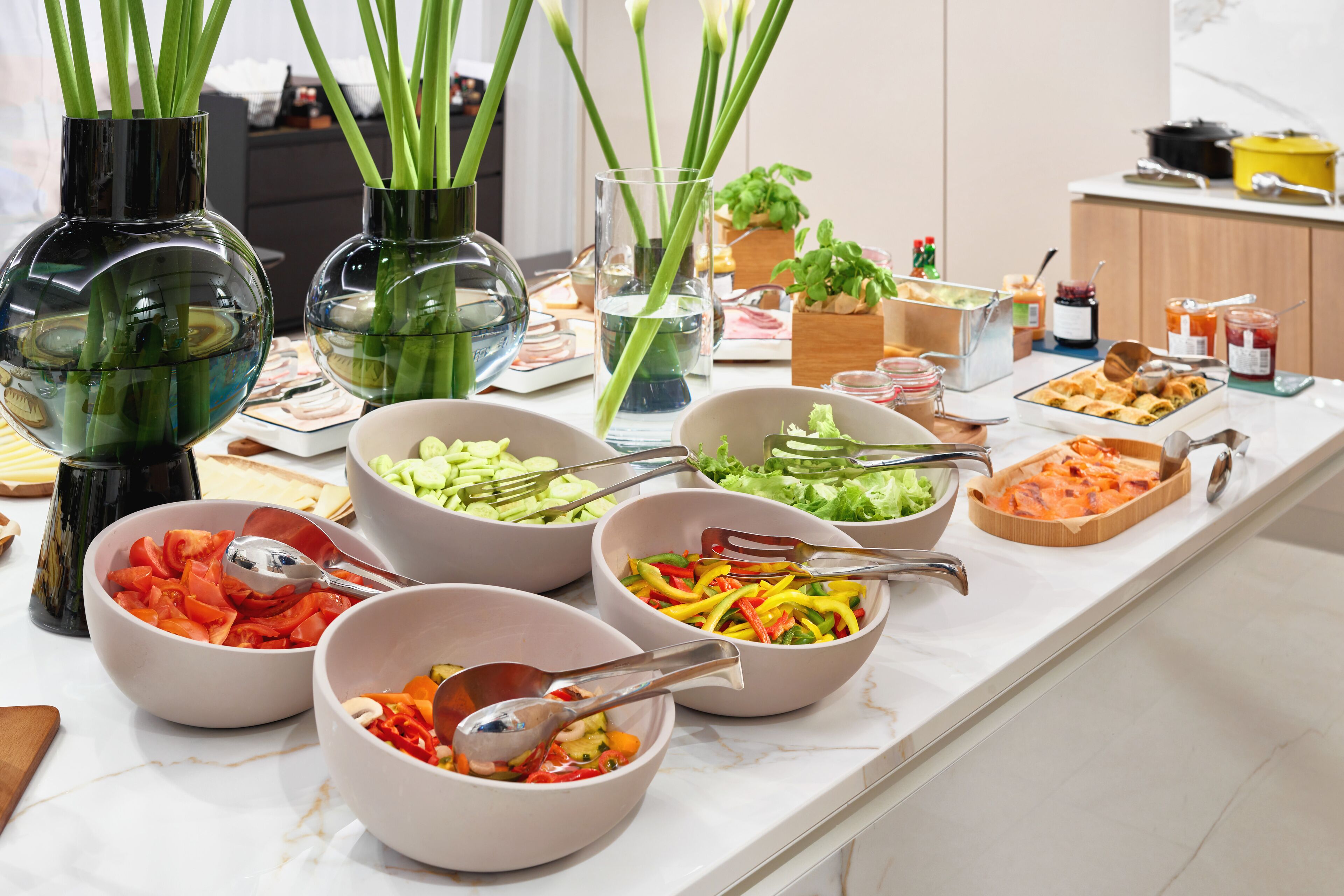A buffet table with various food items and bowls, some with utensils.