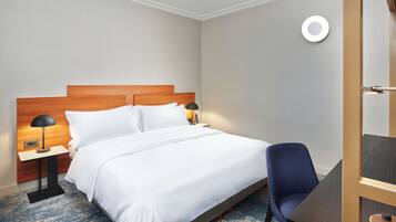 A hotel room with a wooden headboard bed, white bedding, a blue chair, and a small table with a lamp.