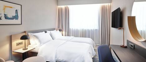 Habitación de hotel con dos camas, un escritorio, una silla, un televisor y un cuadro en la pared.