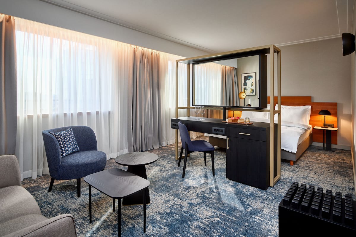 A hotel room with a bed, a desk, a chair, a small table, and a large mirror.