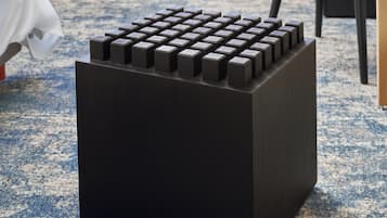 Un objeto negro con forma de cubo y una cuadrícula de botones en la parte superior, sobre un suelo cubierto de alfombra azul.